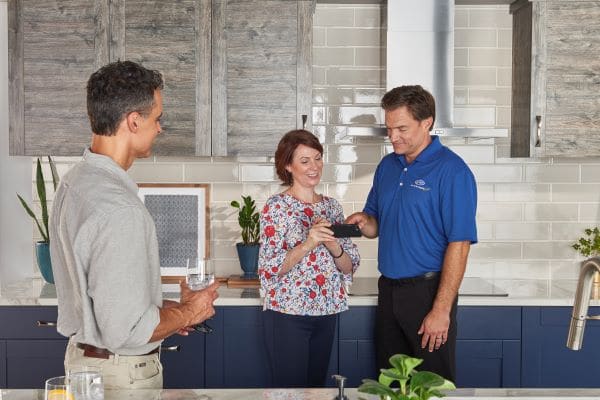 hvac technician showing a man and woman how to operate their air conditioner on phone