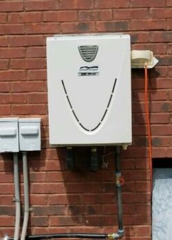 gray tankless water heater installed outside on a brick wall of the building